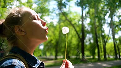 Woman blowing on white dandelion in summer park