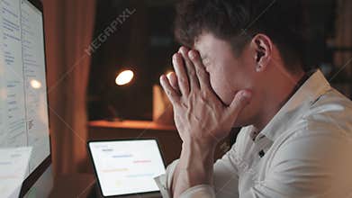 Asian man work late night alone on desktop computer in home office, tired and stressed with work. Overworked, night shift overtime