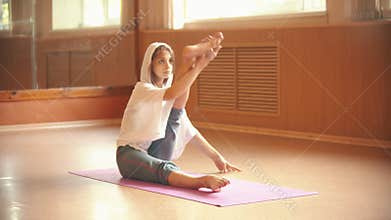 Young woman sitting on the yoga mat and doing leg stretching exercises - dance studio