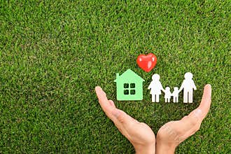 Man holding hands near figures of house, heart and on green grass, top view. Space for text