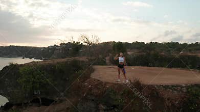Aerial view of woman taking break after exercising on sea shore cliff at sunrise