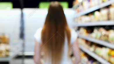 Woman goes into blur through the store with green shopping trolley, between the shelves, supermarket