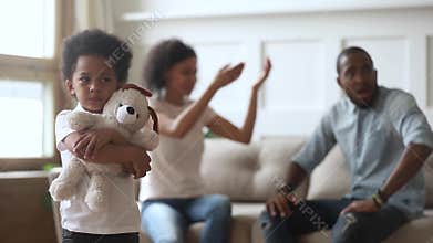 Unhappy little african son embraces toy while parents quarrelling