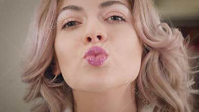 Close-up of charming Caucasian woman applying lipstick, sending air kiss to camera and winking. Happy beautiful girl