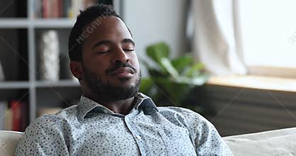 Calm young african man meditate on sofa with eyes closed