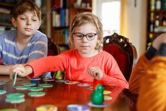 Family playing board game at home. Kids play strategic game. Little sister girl and two school brothers boys. Fun indoor
