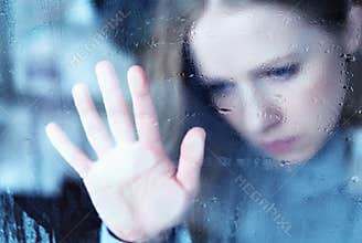 Melancholy and sad girl at the window in the rain