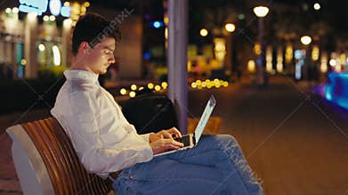 Side View of the Man Distance Working with Wireless Laptop, Typing, Chatting, Browsing in Internet, Sitting Outside at