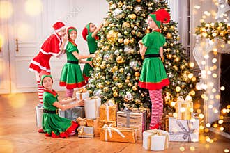 Group of cheerful happy children girls-girlfriends in costumes of elves and Santa with gifts on the background of a Christmas tree