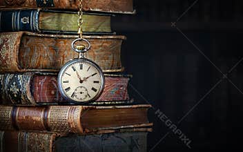 Old clock hanging on a chain on the background of old books. ?lock as a symbol of time a books are a symbol of knowledge..