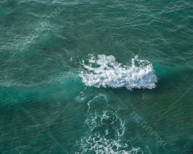 Ocean foamy waves approaching rocky shore. Top view