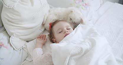 Adorable one-year-old girl sleeping peacefully with a sweet Bichon Frise