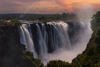 Aerial view of Mosi-Oa-Tunya Falls waterfall in Zambia during sunset with birds flying around