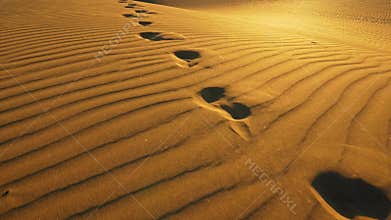 Camera follows footprints in big sand dune. Footprints in the sand in desert at warm sunset lights. UHD, 4K