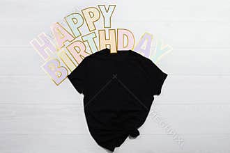 Happy birthday holiday celebration. Summer black b-day t shirt mockup flat lay isolated. White wooden background. Top front view t