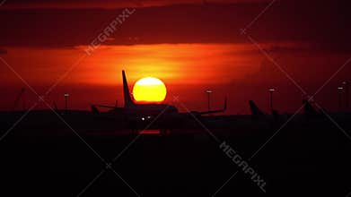 Bali, 30 Apr 2019: An airplane taxis along the runway at Ngurah Rai Airport, Bali, with a stunning fiery sunset illuminating the