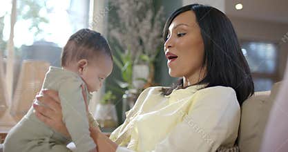 Mother and daughter practicing standing after adjusting under arms by lifting child on sofa at home