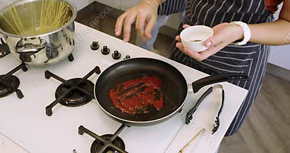 When pasta boils Diverse women cooks stirring sauce and adding sliced carrots in kitchen copy space