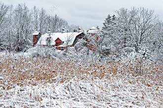 Winter white snow on red barn with silo and field or meadow