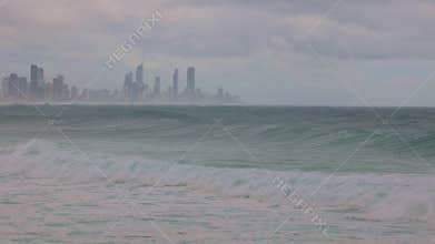 Heavy swells and waves generated by a cyclone or hurricane with a city in the background.