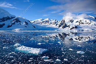 Snowcapped mountains in beautiful landscape, reflecting in blue water, ice flows, Lemaire Channel near Paradise Bay, Antarctica