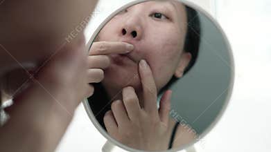 Worried Young Asian Woman Examining Skin In Mirror. Acne Concern, Skin Problem Awareness, Acne Treatment.