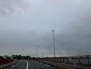 Curved urban roadway on rainy overcast day with tall streetlights, red bridge