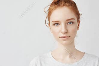 Close up portrait of young beautiful redhead girl in white shirt smiling looking at camera. Copy space. Isolated on