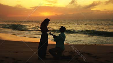 Young Man Proposing To Woman Sunset-Lit Beach