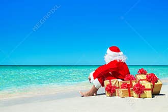 Christmas Santa Claus with gift boxes relaxing at ocean beach