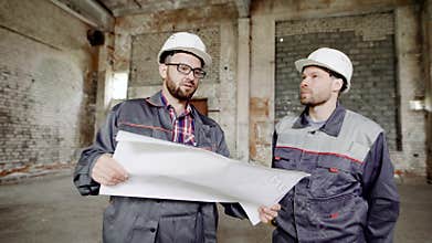 Two men, who builders in a protective helmet on their heads and special clothes look at the factory building in order to