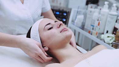 Close up view of a young professional cosmetologist making a plastic facial massage to a beautiful female patient
