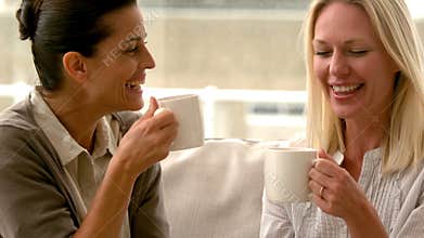 In slow motion two friends sitting on the couch chatting over coffee at home