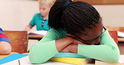 Little girl sleeping on a book in classroom