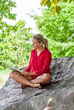 Smiling 20s girl reading a summer book under a tree