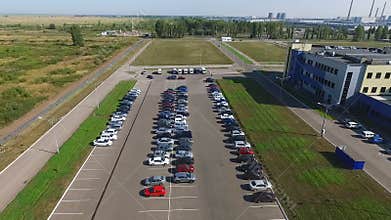 Video from drone that flies along the parking. A large number of parked cars stand near the factory.