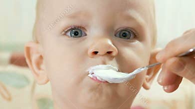 Attractive baby eats cottage cheese with spoon using mothers. Kid 1 year. Close-up