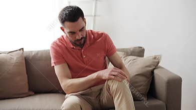 Unhappy man suffering from pain in leg at home