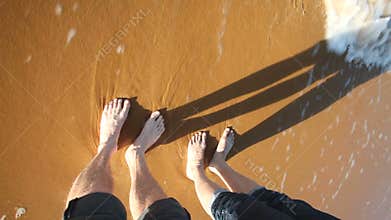 Sea waves splashing woman and man's legs on sandy beach