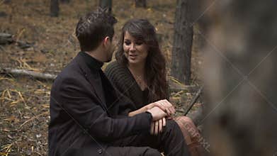 Close up of happy couple is having a date in the forest. Smiling man and woman are sitting on the log in the forest