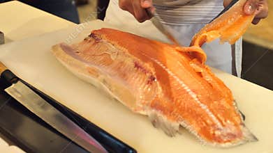 Close-up of sushi chef show one`s capability slices fresh salmon at sushi bar.