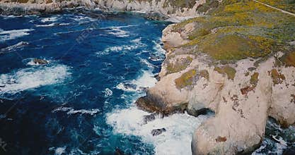 Drone flying high above beautiful ocean shore, foaming waves crash over large rocks at summer Big Sur scenery California