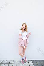Portrait of a full-length lady in pink dress and a white T-shirt standing against a white wall