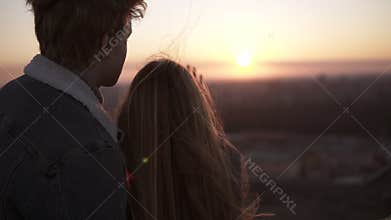 Young woman with long hair standing with her boyfriend on the roof and touching the sunlight by hand over beautiful sky