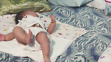 Asian baby girl lies on a bed and learning to roll from back to stomach.