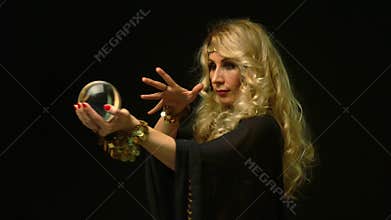 Beautiful blond astrologer woman looking through crystal ball.