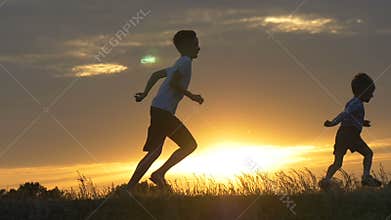 Silhouettes of running children in a field at sunset