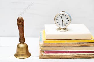 Old school bell and old clock on a pile of old books. Vintage