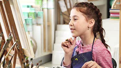 Cute little girl showing thumbs up while painting a picture at the art class