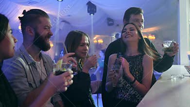 Men and young women with colorful cocktails make a toast and have good time near the bar counter in nightclub